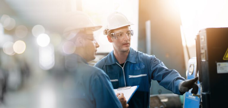 Industrial workers in safety gear analyzing machinery in a factory setting.